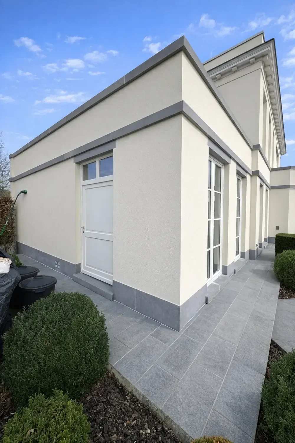 Dezelfde villa-aanbouw na softwash: egaal crèmekleurige crepi rond arduin en wit schrijnwerk