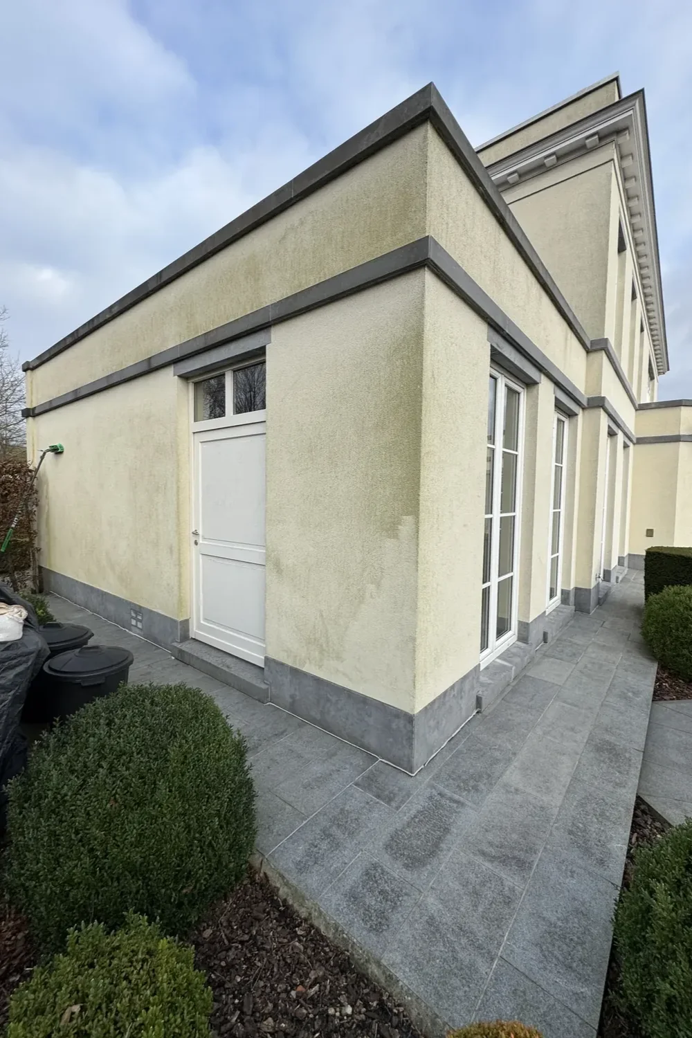 Crèmekleurige crepi met groengele aanslag op de aanbouw van een villa, vóór reiniging
